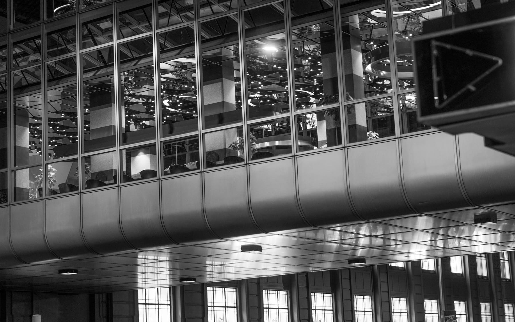 A monochrome view across an interior mezzanine toward a tall glazed wall.